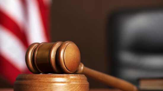 Wooden gavel on the table of judge with american flag and black chair
