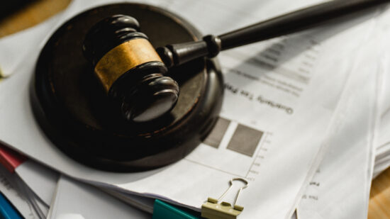 Wooden gavel rests on documents. Paperwork piles beneath a judge's hammer. Clips and pens lie nearby, ready for use. Legal matters feel urgent and serious. Ideal for law, finance, or courtroom themes